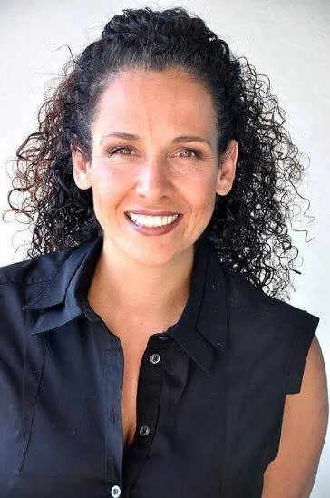 Sunita Shroff: A woman with curly dark hair smiling, wearing a black shirt.