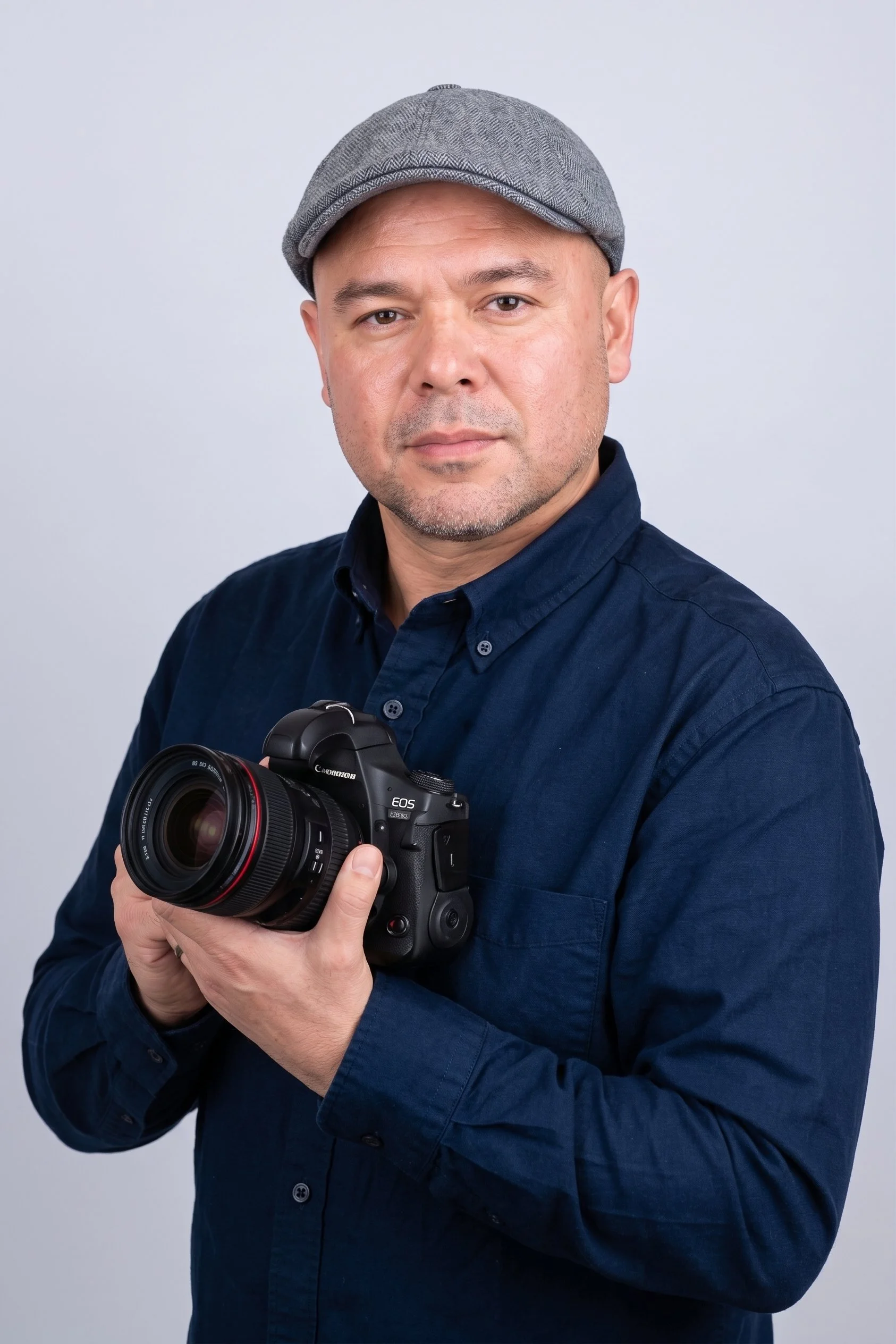 Matt Chung Photography - A man wearing a gray flat cap and navy blue shirt holding a Canon EOS camera against a plain light gray background.