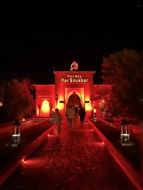 Night view of Palais Dar Soukkar illuminated in red with people walking towards the entrance