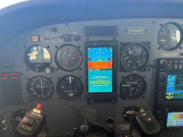 Aircraft cockpit instrument panel with avionics, gauges, and a central digital display showing flight information.
