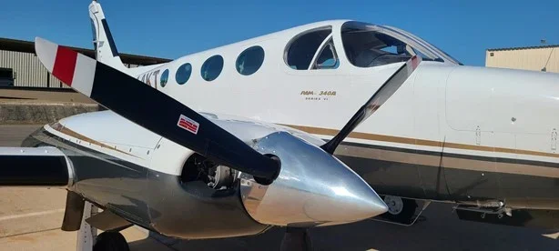 A small private jet with a white body and gold accents parked on the tarmac, showing part of the fuselage and propeller.
