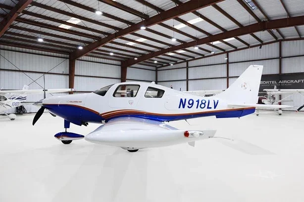 Small private aircraft with white, blue, and red coloring inside a hangar.