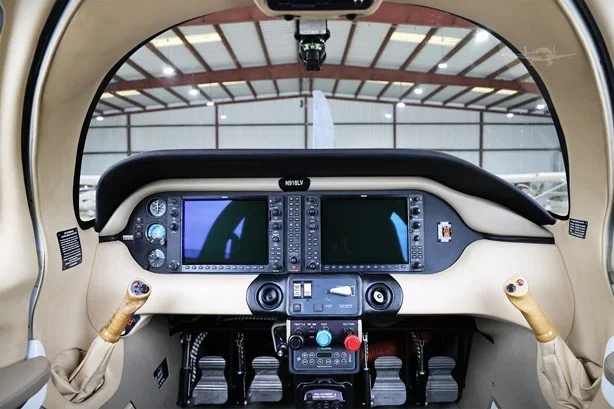 The interior cockpit of a small aircraft, featuring two control yokes, two digital displays, and various switches and controls.