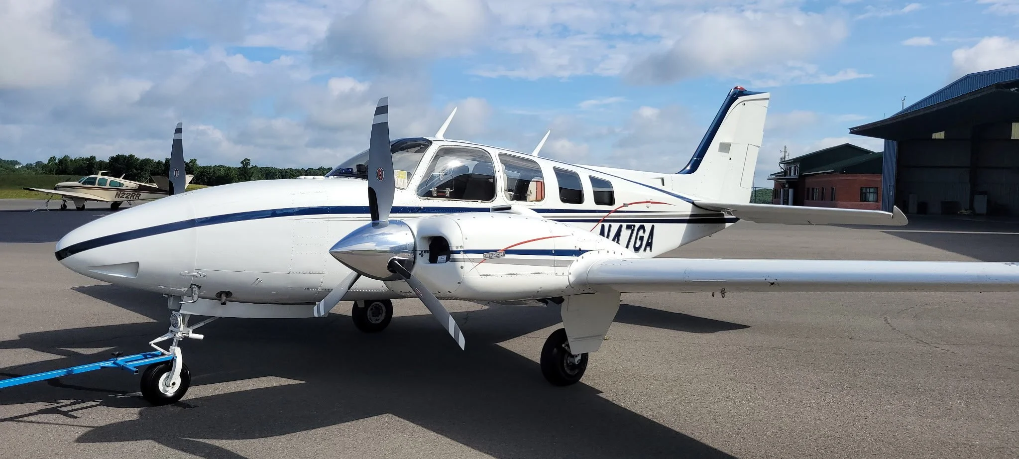Small white private jet with blue stripes parked on tarmac, with a smaller aircraft in the background and a building nearby.