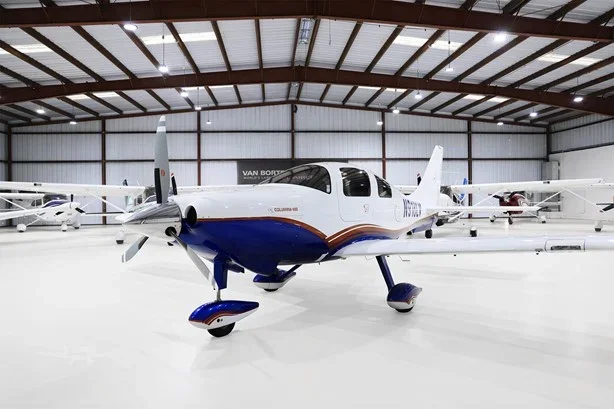 Single-engine propeller aircraft inside a spacious hangar with other small planes.