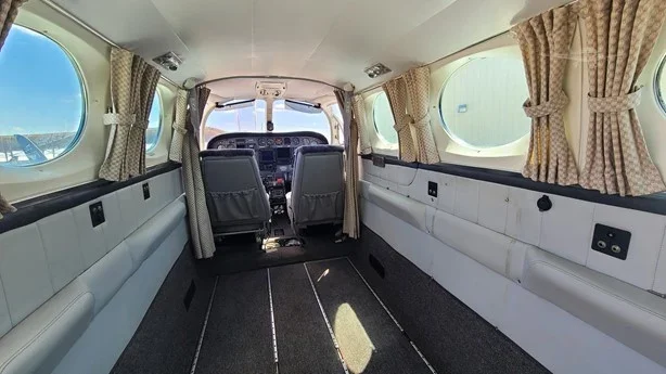 Interior of a small airplane with two front seats, side windows with curtains, and a spacious cargo area behind the seats.