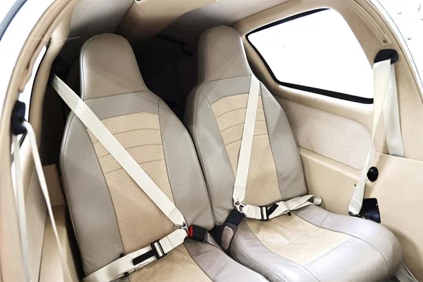 Interior of a small aircraft showing two beige and gray passenger seats with seat belts.