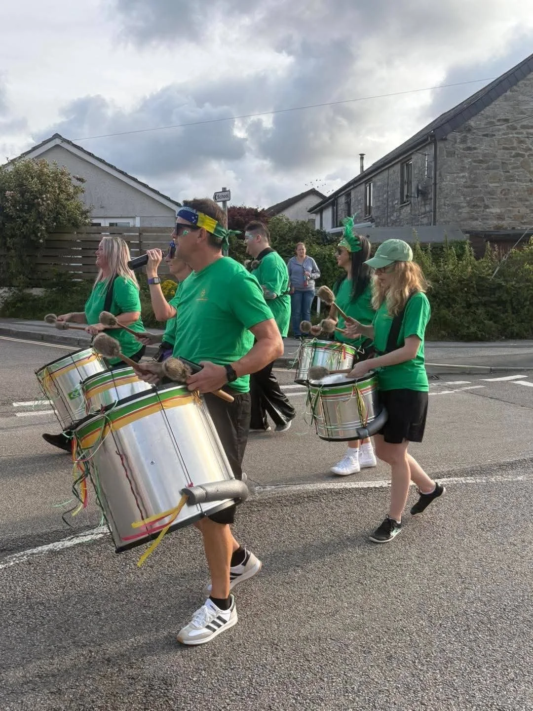 Group of people dressed in green playing drums while walking on the street during a parade or celebration.