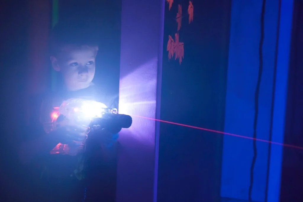 A child holding a laser tag gun, with a blue laser beam extending from the gun across the image in a dark room.
