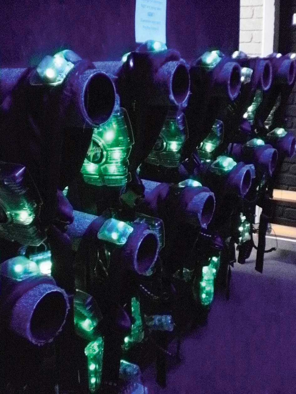 Row of black laser tag vests with green LED lights in a dark room.