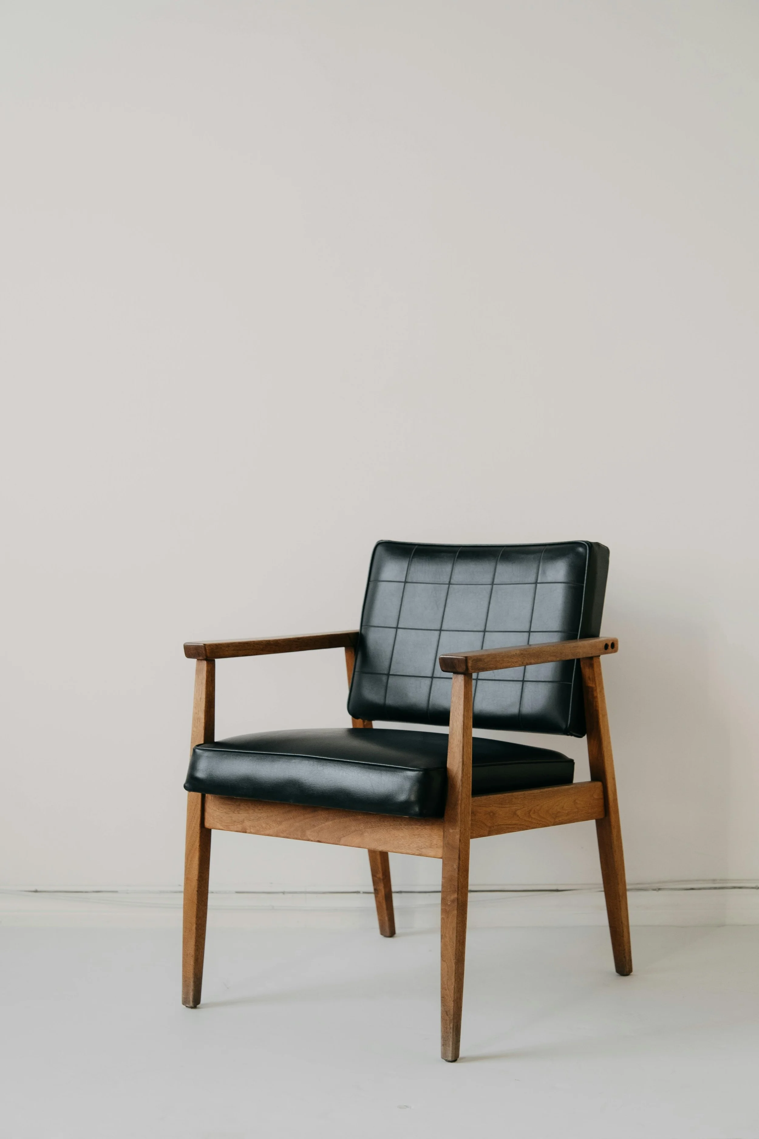 A black and wooden armchair with a cushioned seat and backrest, placed against a plain white wall.