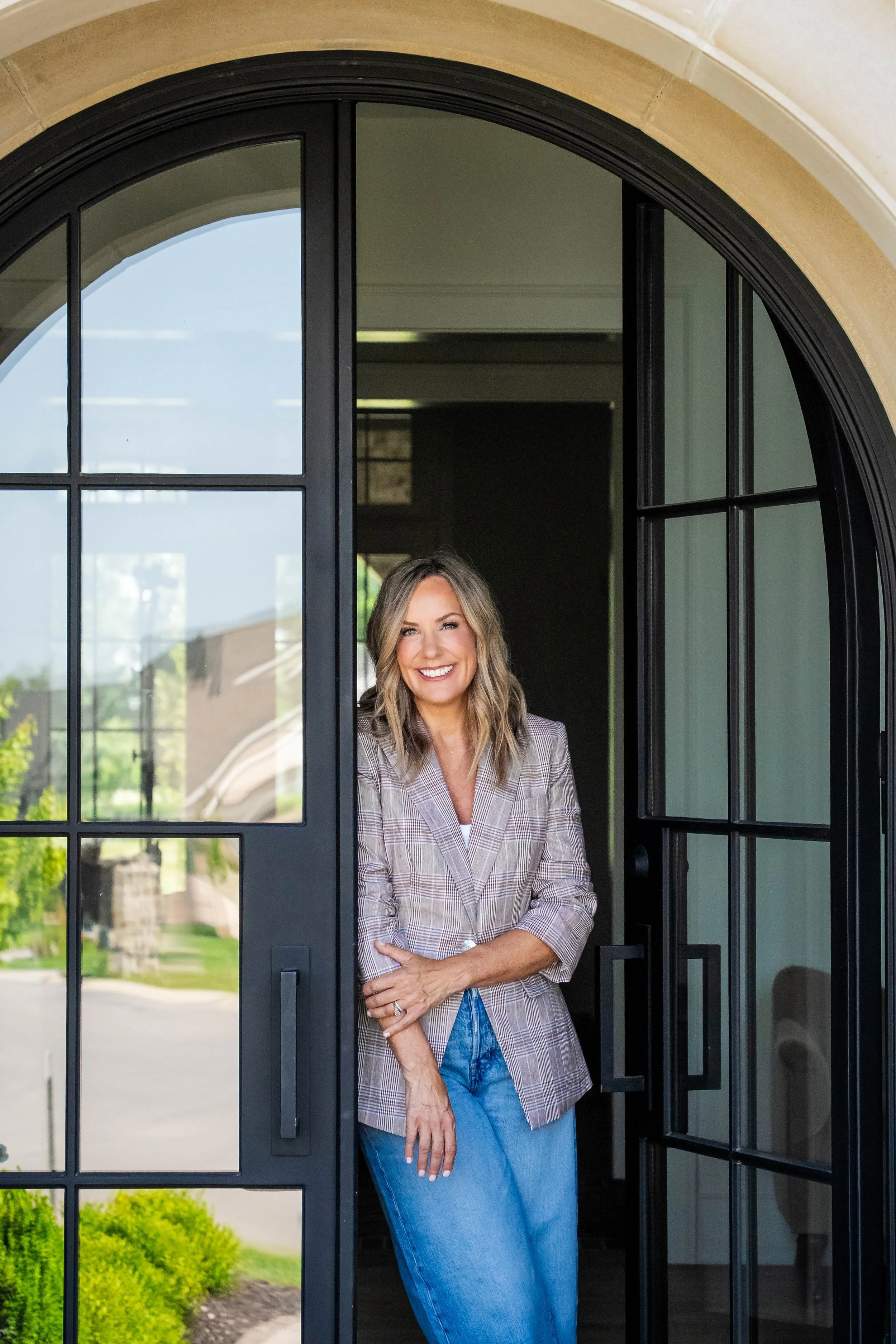 Owner and Principal Designer, Jodi Pierrot, standing in an arched doorway of one of her custom home designs in Indiana.