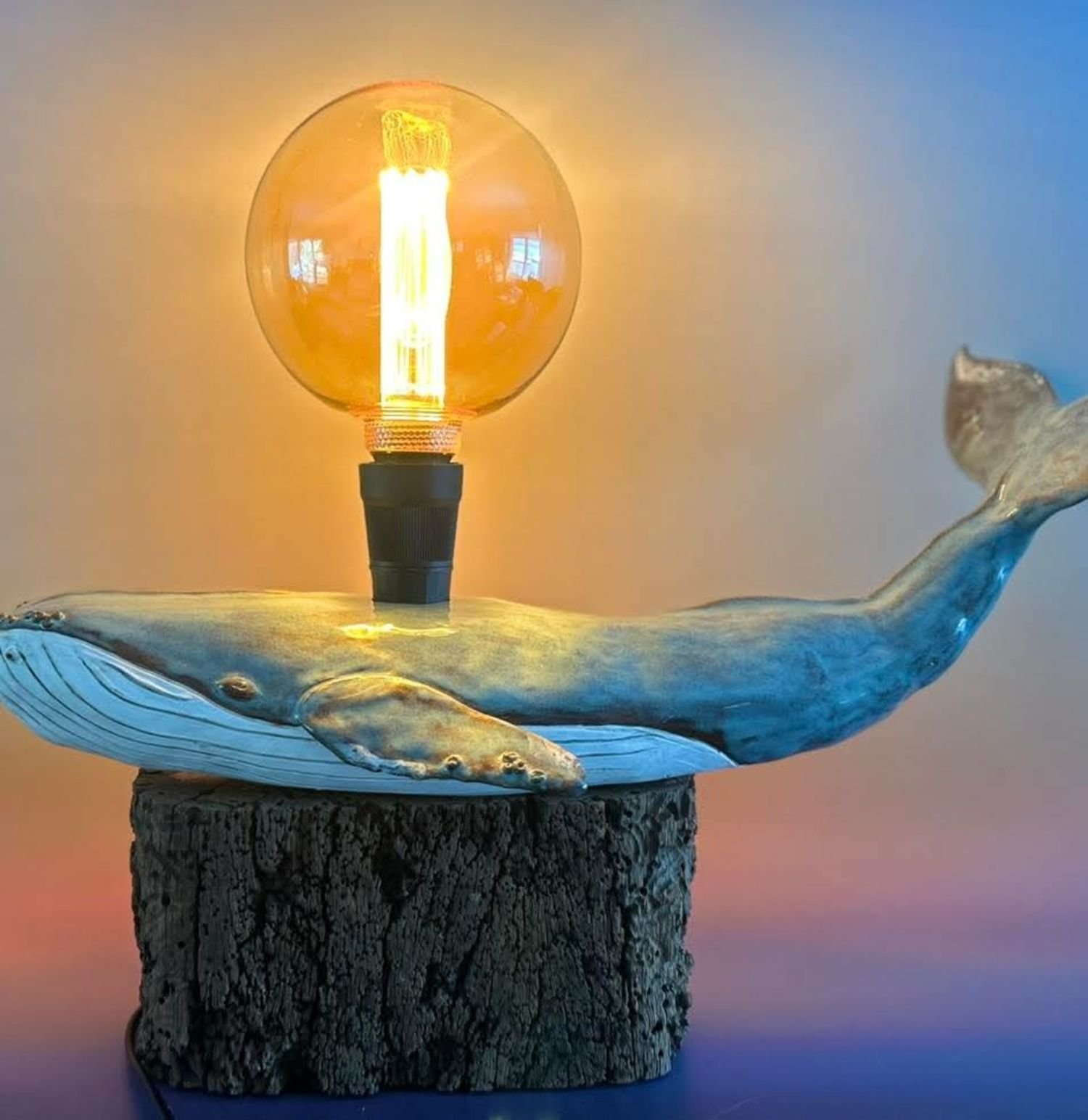 A decorative light bulb designed like a whale with water splashing from its blowhole, placed on a wooden base.