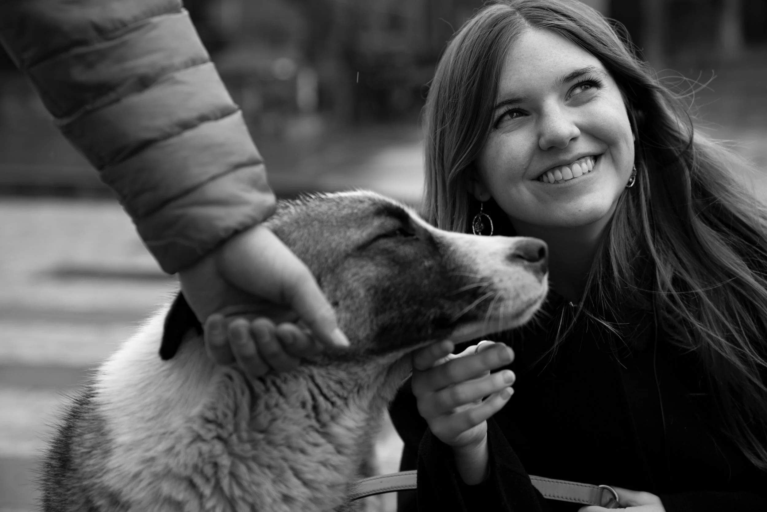 A woman smiling and petting a dog outdoors, black and white photograph.