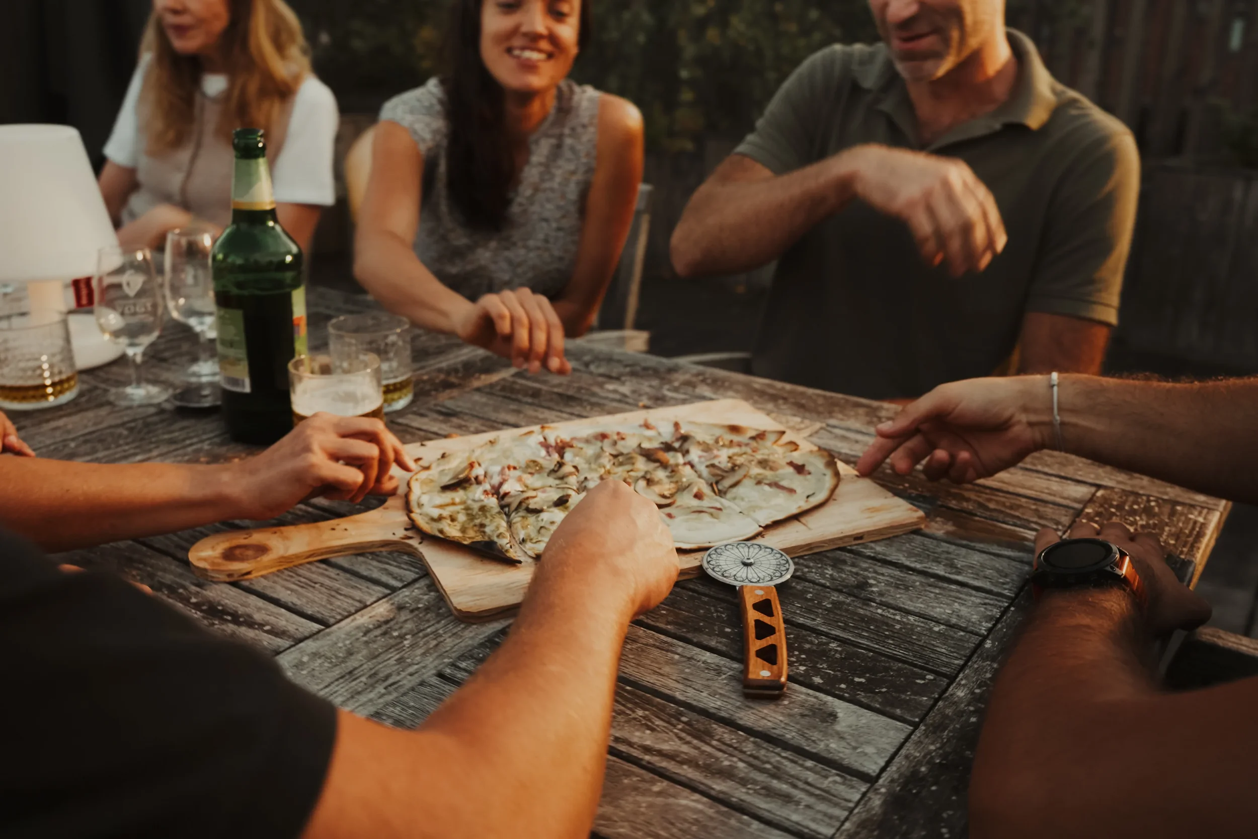 Groupe de personnes partageant une pizza faite maison lors d'un repas en plein air le soir.