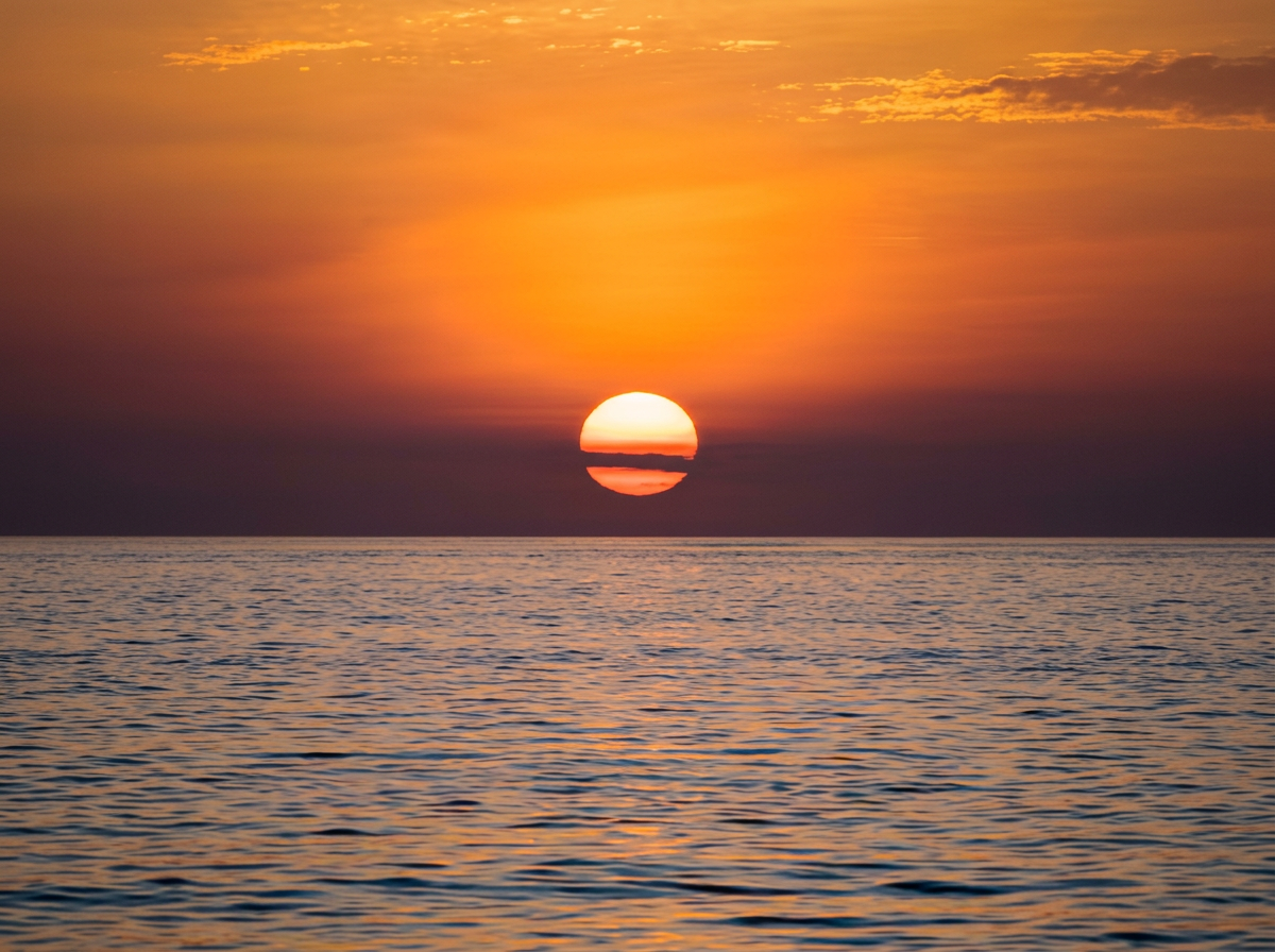 Coucher de soleil sur l'océan avec le soleil partiellement visible à l'horizon, ciel orange et reflet sur l'eau.