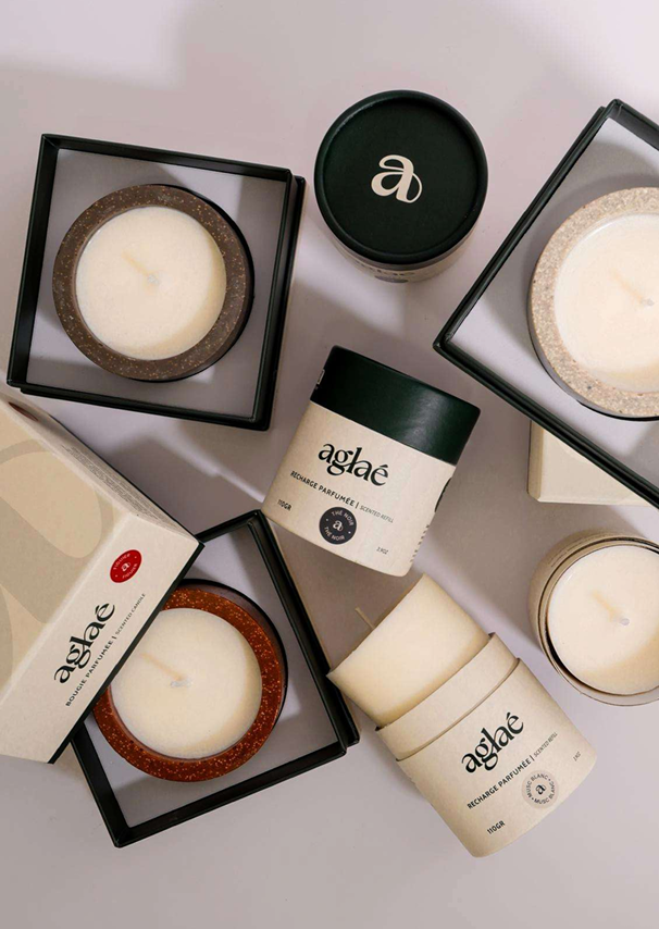 Bougies parfumées en boîte et en pot, certaines dans des boîtes noires et blanches, disposées sur une surface blanche.