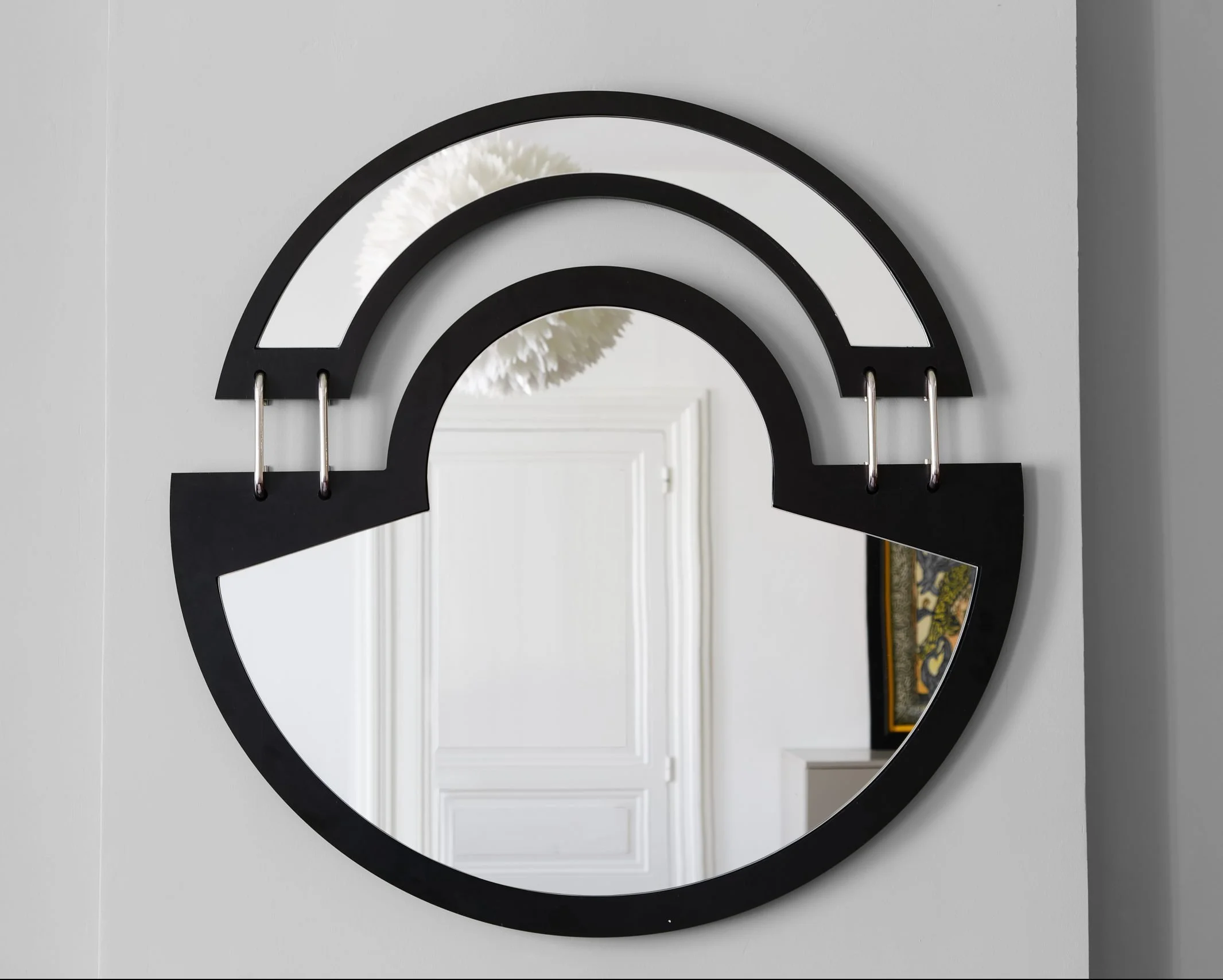 Miroir en forme d'arc noir fixé au mur, avec une décoration végétale blanche visible dans le reflet.