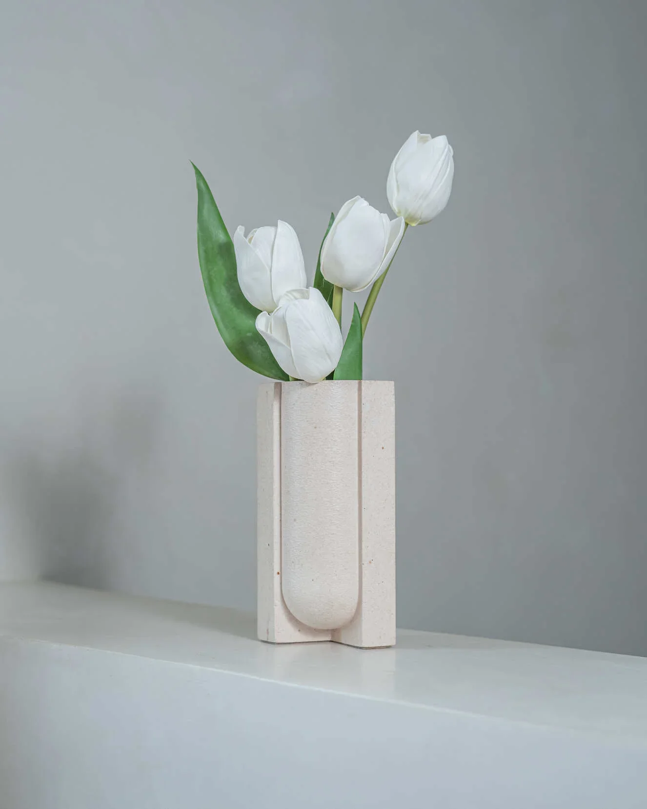 Vase en céramique blanche avec des tulipes blanches et une feuille verte sur un fond gris
