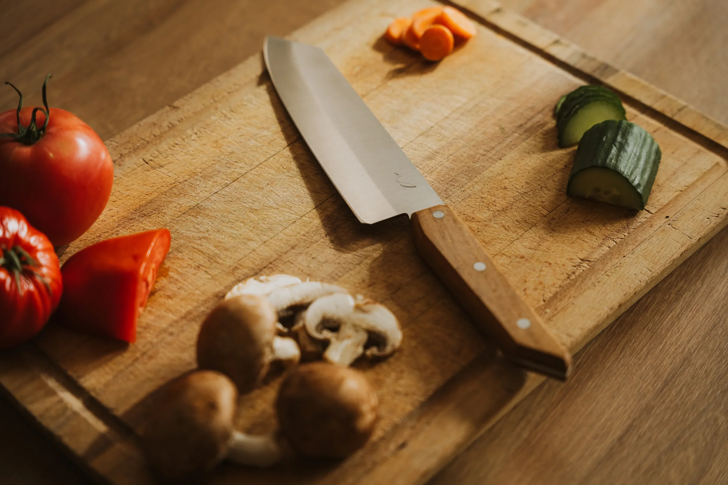 Mandoline en bois avec des tranches de concombre, de la tomate et des champignons autour.