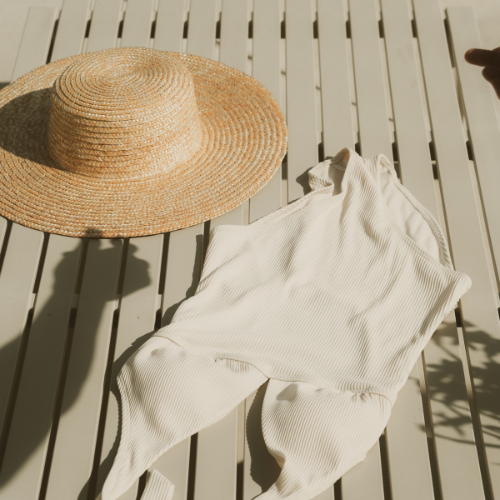 A straw sun hat and white clothing laid out on a wooden deck with shadows from nearby plants or trees.