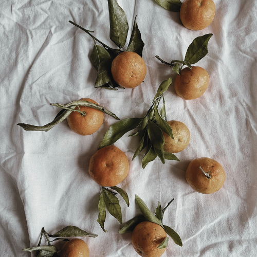 Fresh oranges with green leaves on a white crumpled cloth background.