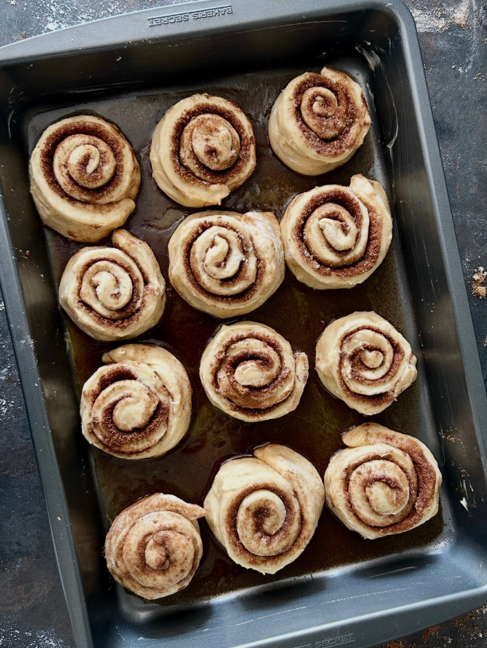 Baking tray with uncooked cinnamon rolls topped with cinnamon sugar swirl.