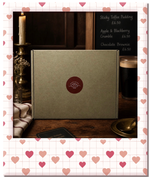 A gray gift box with a red circular sticker featuring a whale, on a wooden table with a brass candle holder and candle, a black chalkboard menu, and a pint of dark beer, in a cozy cafe setting.