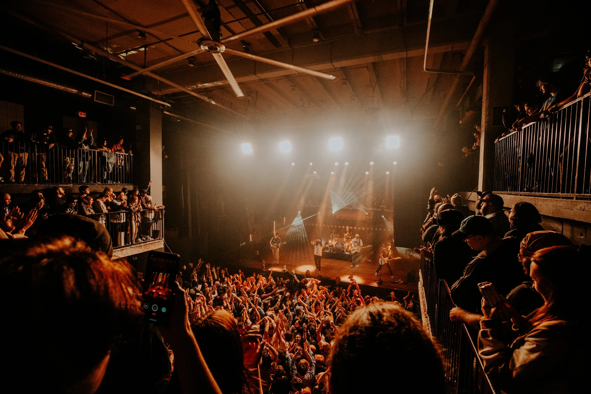 Crowd at a concert with band performing on stage and colorful lighting effects.