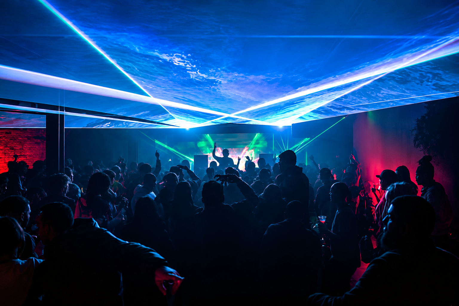 A large crowd dancing and enjoying a concert or club with colorful lighting, laser beams, and a DJ or performer on stage.