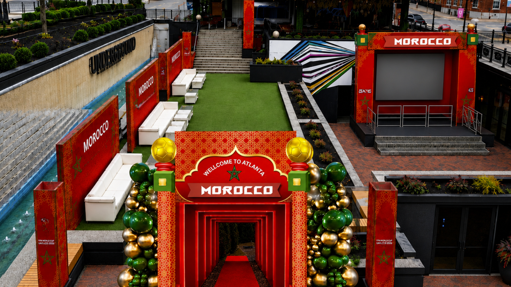 Decorative entrance with red archway and festive balloon decorations, surrounded by seating, greenery, and a small stage area, welcoming visitors to Morocco in Atlanta.