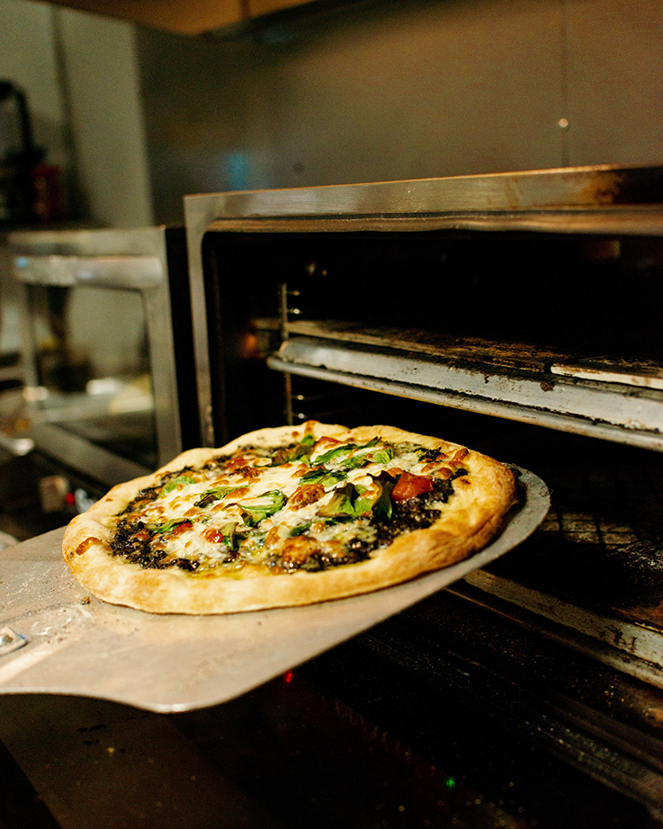 Freshly baked pizza being removed from an oven, topped with vegetables and cheese.