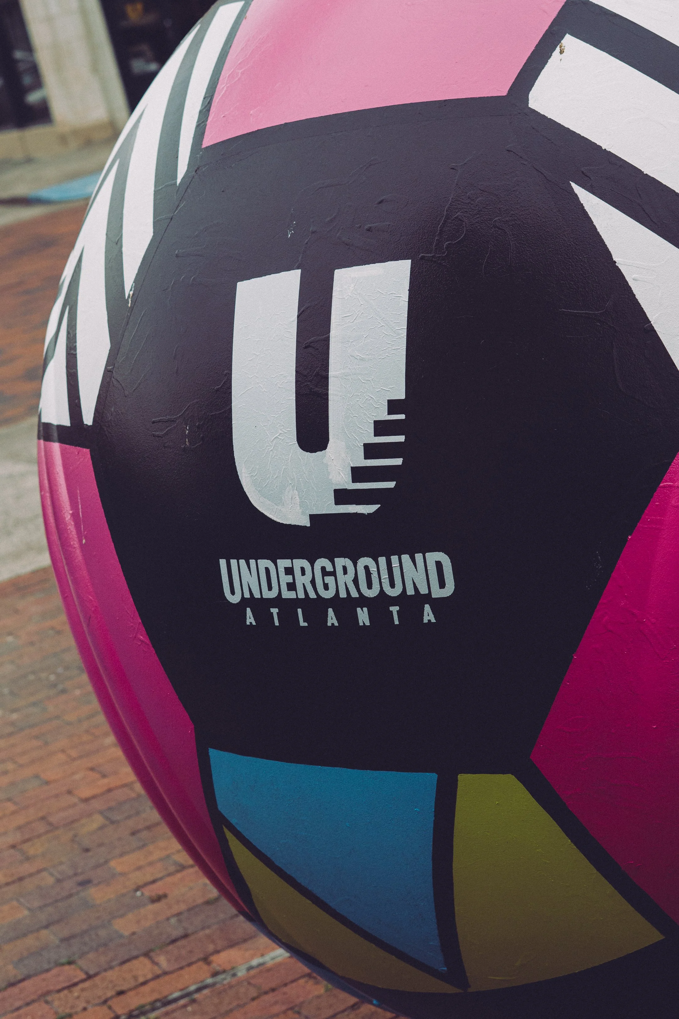 Close-up of a pink, black, yellow, and blue painted ball with the words "UNDERGROUND ATLANTA" written on it.