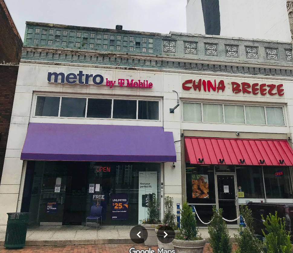 Facade of a building with signs for Metro by T-Mobile and China Breeze, featuring storefronts with awnings and plants outside.