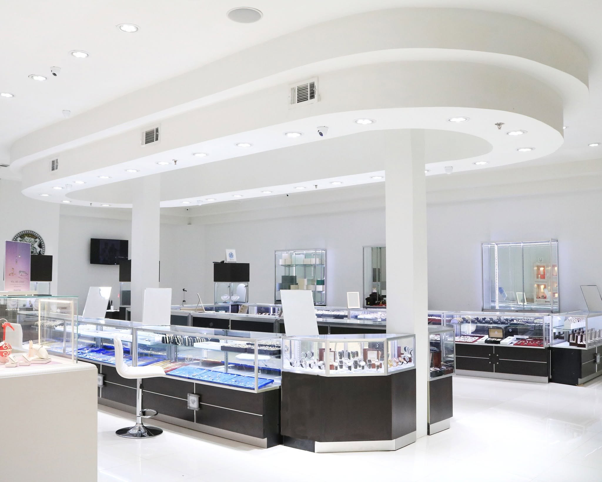Jewelry store interior with display cases filled with jewelry and watches, white walls, and ceiling with multiple recessed lights.
