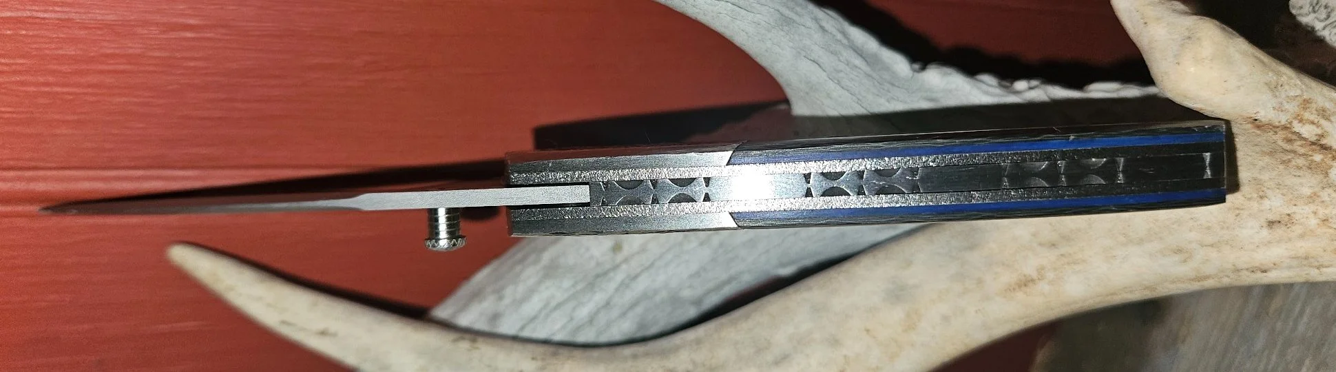 Spine view of B.A. Dodson carbon fiber and tooled titanium liner lock folder showing blue liners and decorative backspacer filework