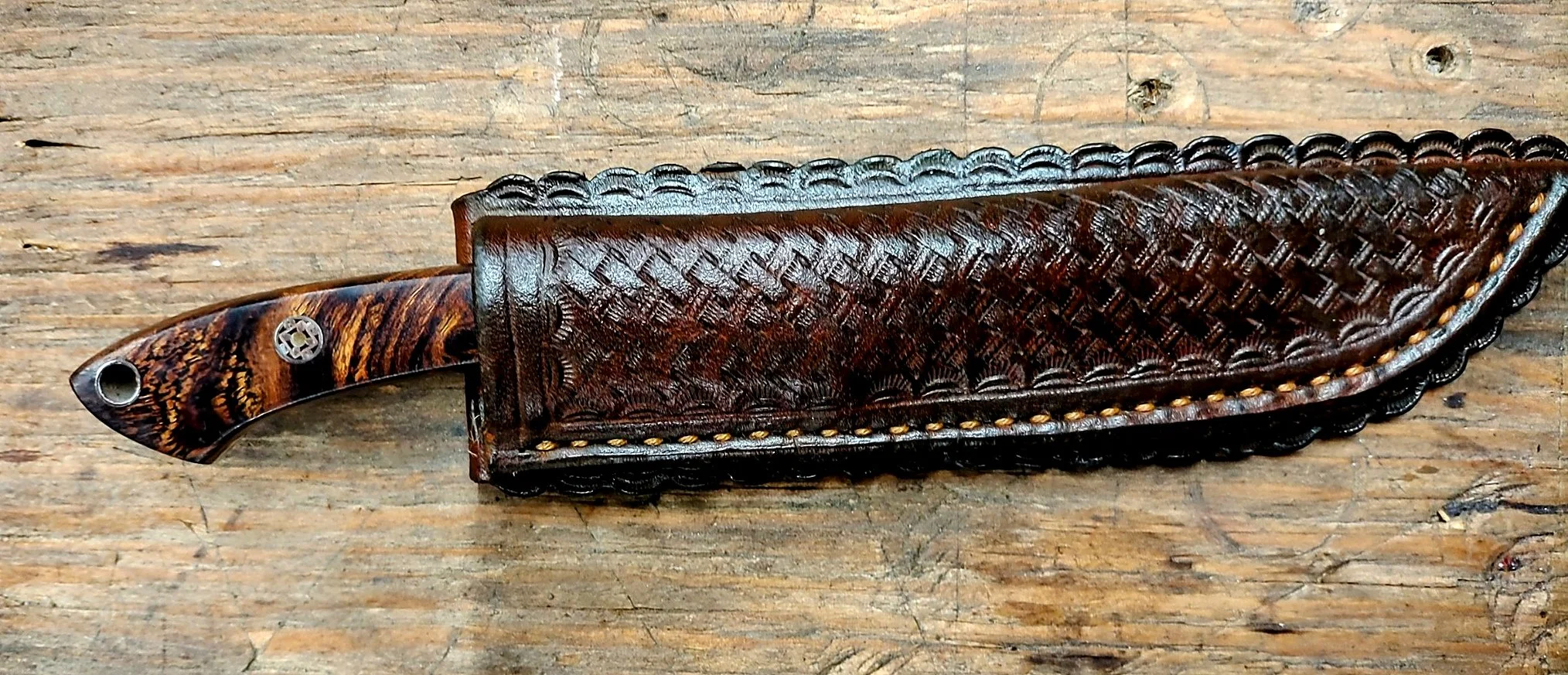 B.A. Dodson Desert Ironwood fixed blade partially sheathed in a custom hand-tooled basketweave leather sheath with decorative border work and hand stitching.