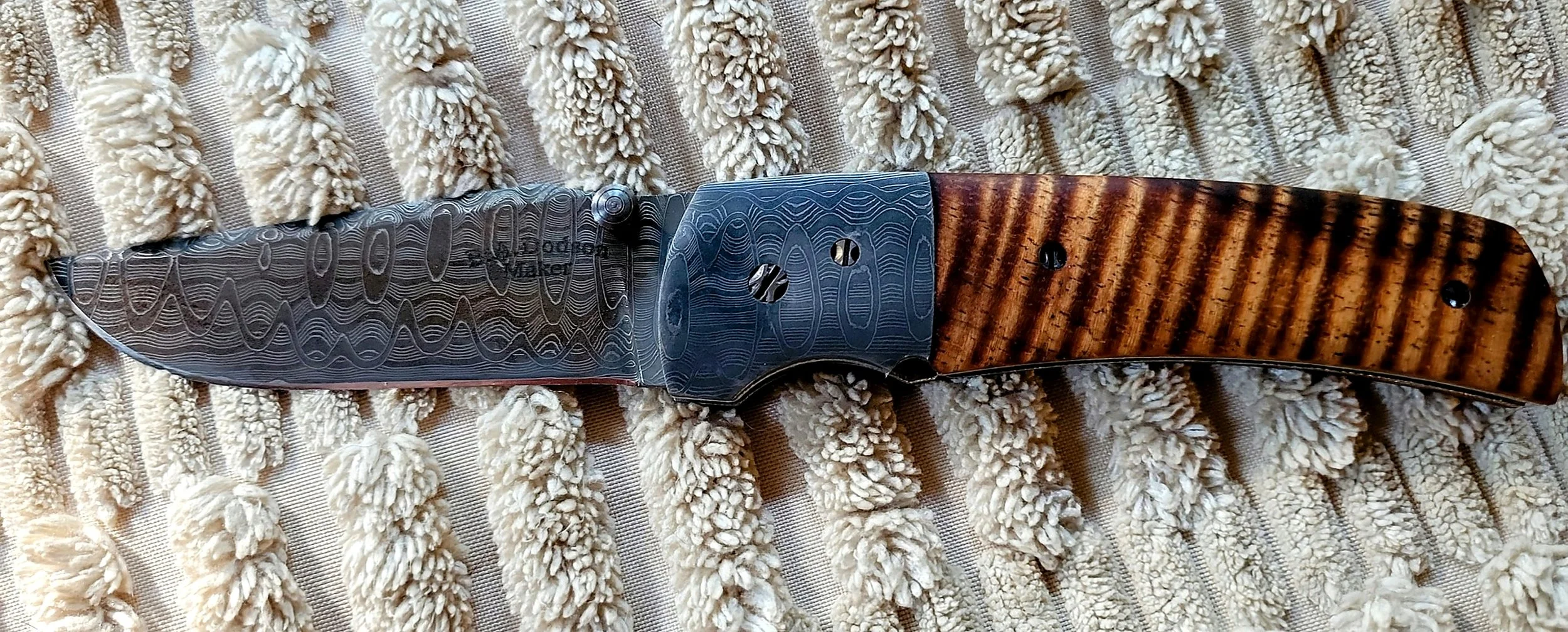 B.A. Dodson Koa & Damasteel folder with Damasteel Damascus blade and bolster, koa handle scales, and decorative hardware.