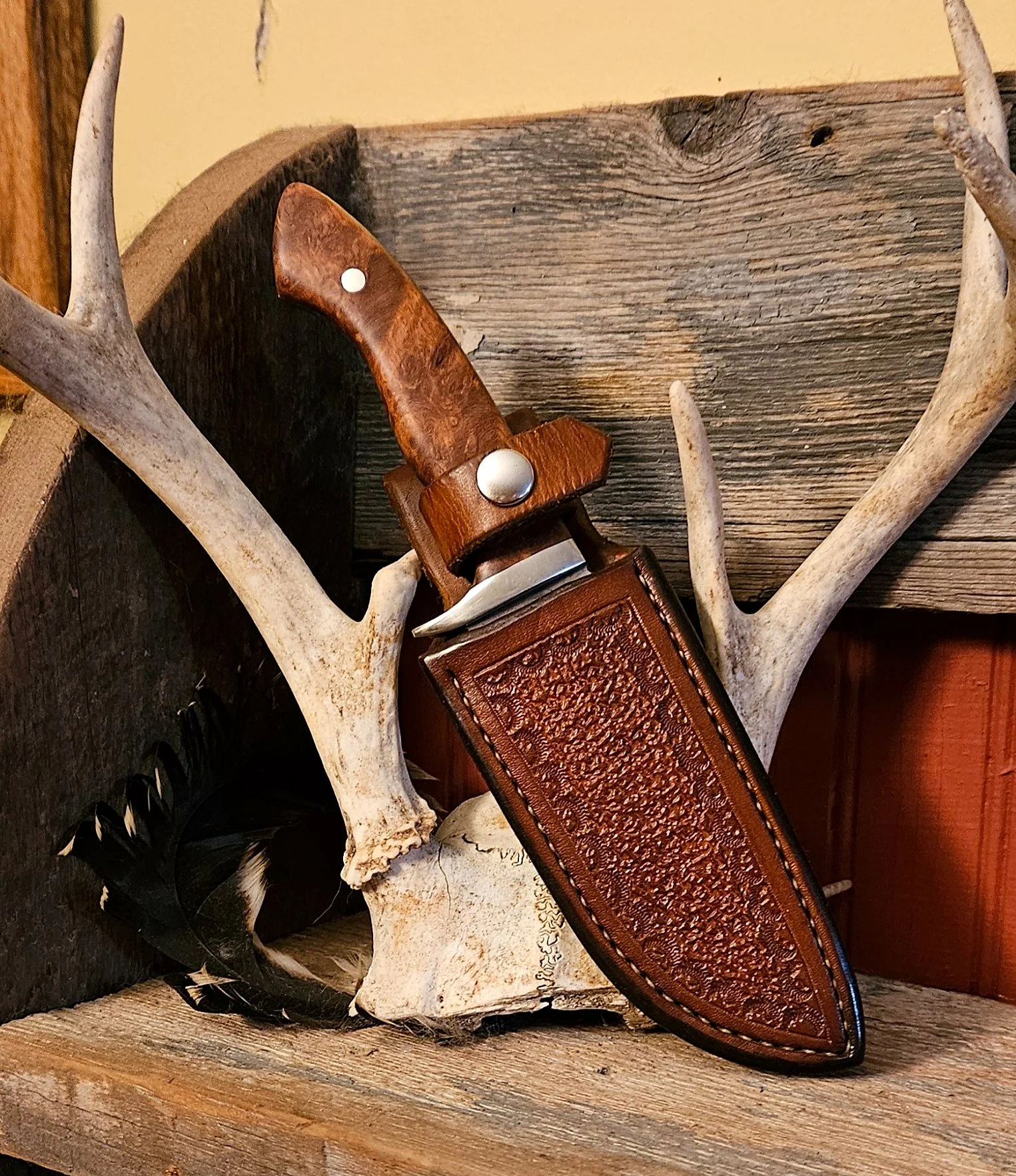 B.A. Dodson presentation-grade wood fixed blade partially sheathed in a custom hand-tooled leather sheath with decorative stamping and hand stitching