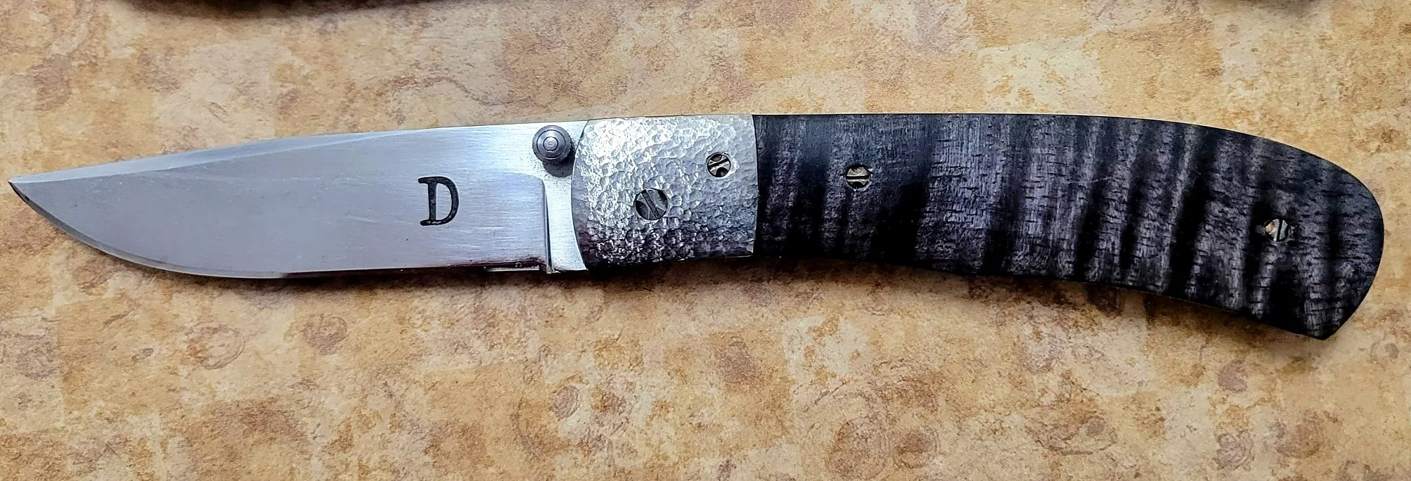 B.A. Dodson maple and titanium folder with dark figured maple handle scales, textured titanium bolster, and satin-finished blade.