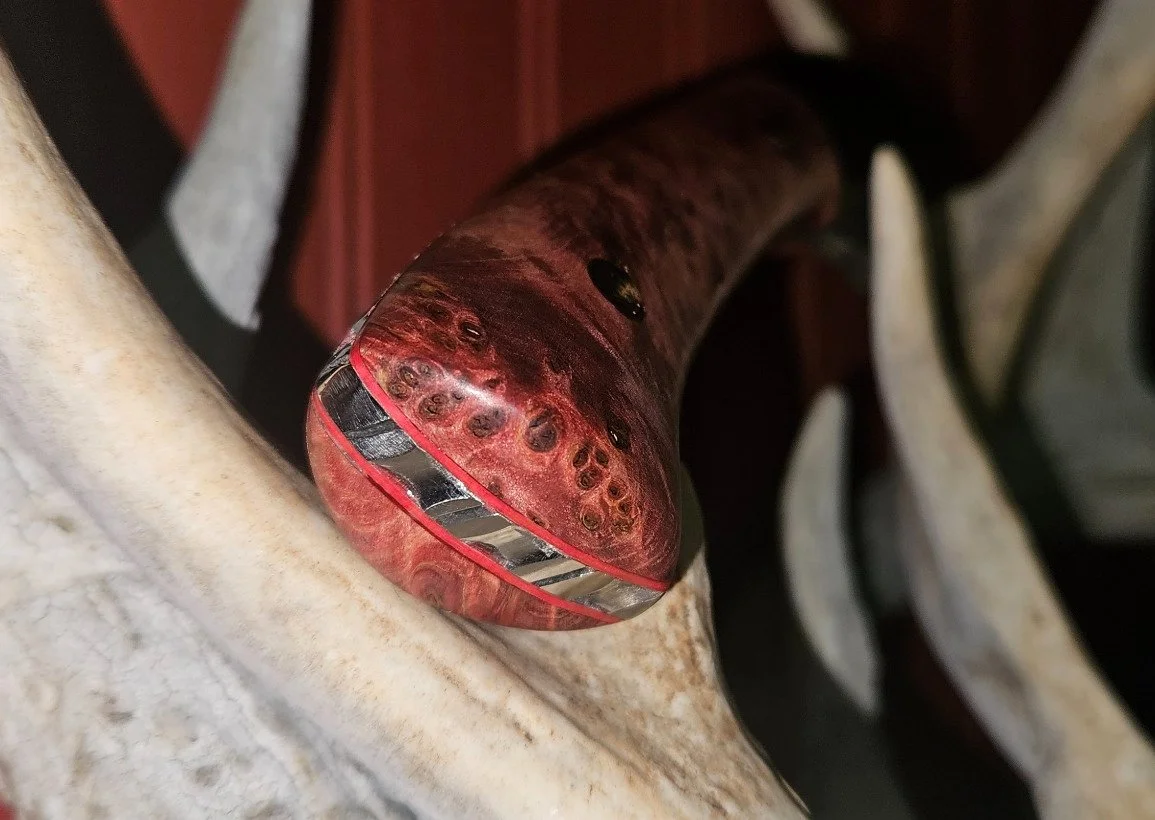 Handle butt detail of a B.A. Dodson presentation wood fixed blade showing decorative filework and red liners.