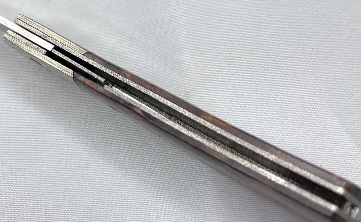 Interior spine view of a B.A. Dodson compact cottonwood and mokume liner lock folder showing the lockup and liner construction on a white cloth background.