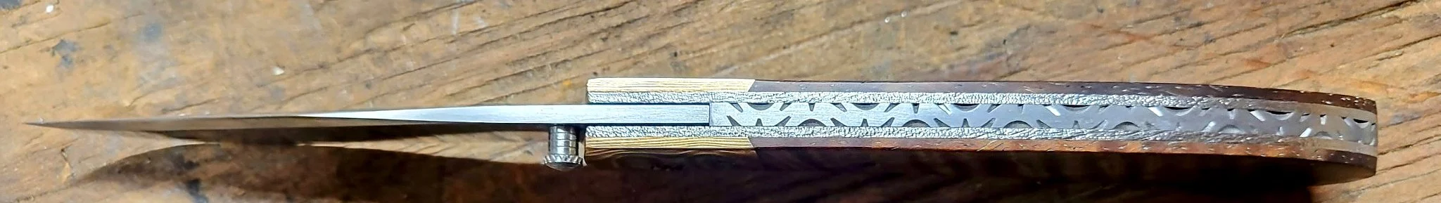 Alt text: B.A. Dodson Koa and Mokume liner lock folder viewed from the spine, showing decorative backspacer file-work and liner construction.