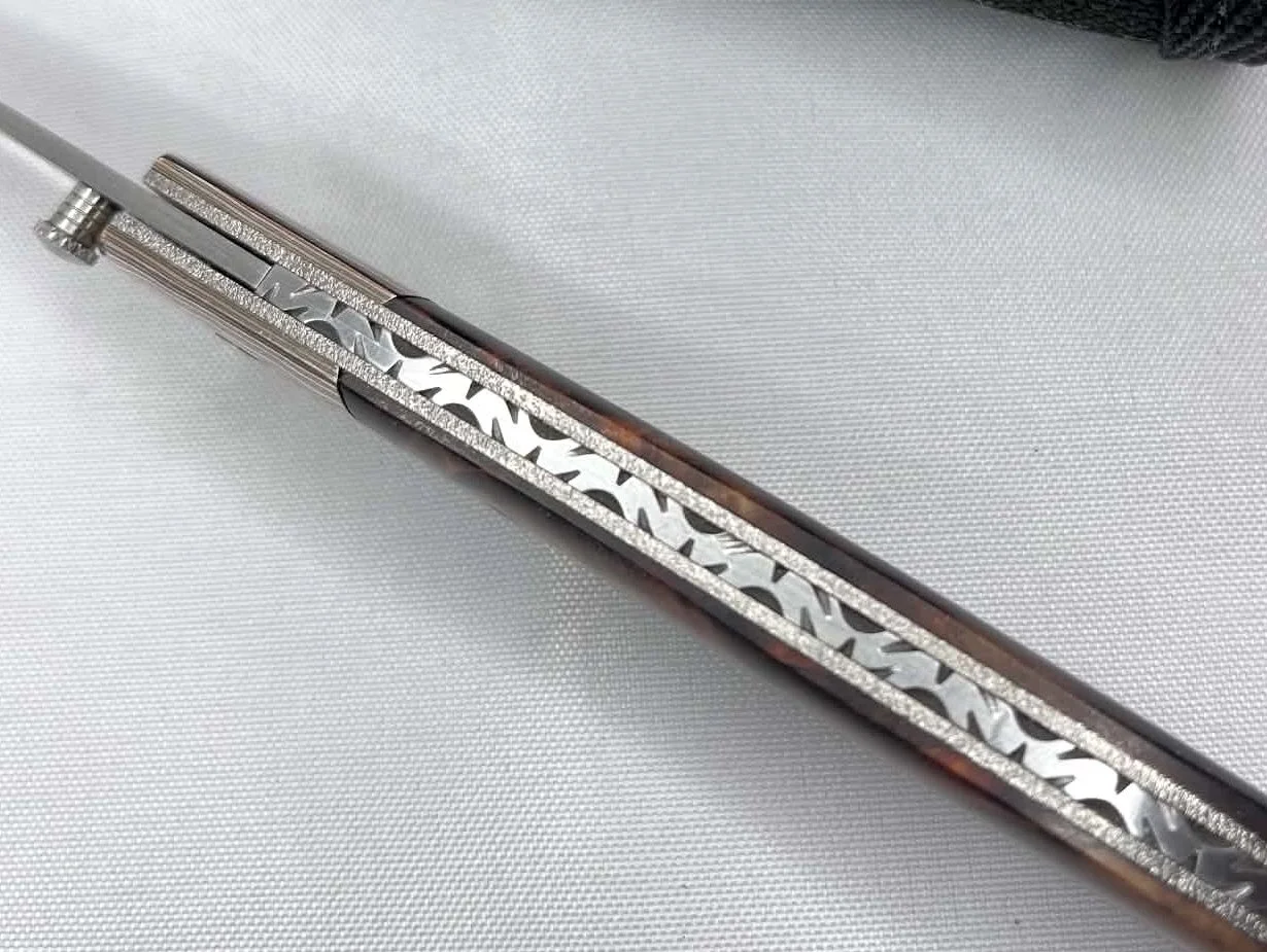 Spine view of a B.A. Dodson compact cottonwood and mokume liner lock folder showing decorative backspacer filework on a white cloth background.