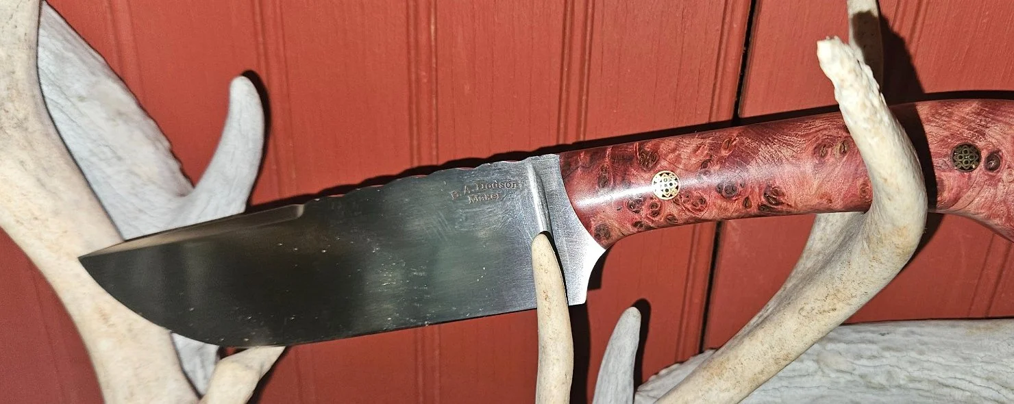 Opposite-side view of a B.A. Dodson presentation wood fixed blade displayed on antlers, showing the figured wood handle and satin-finished blade