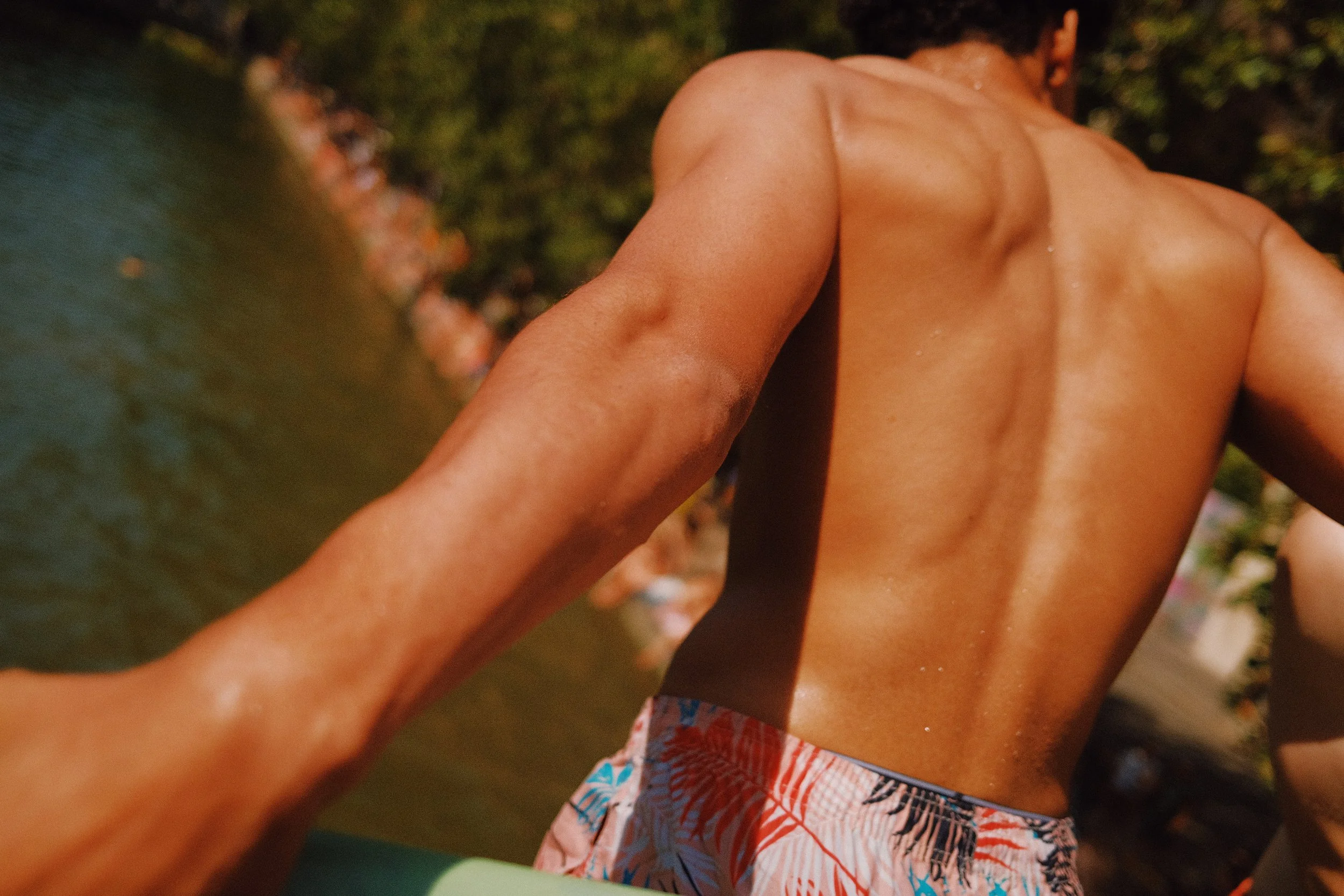Enfant en maillot de bain coloré, vu de dos, dehors, arrière-plan flou avec des arbres.