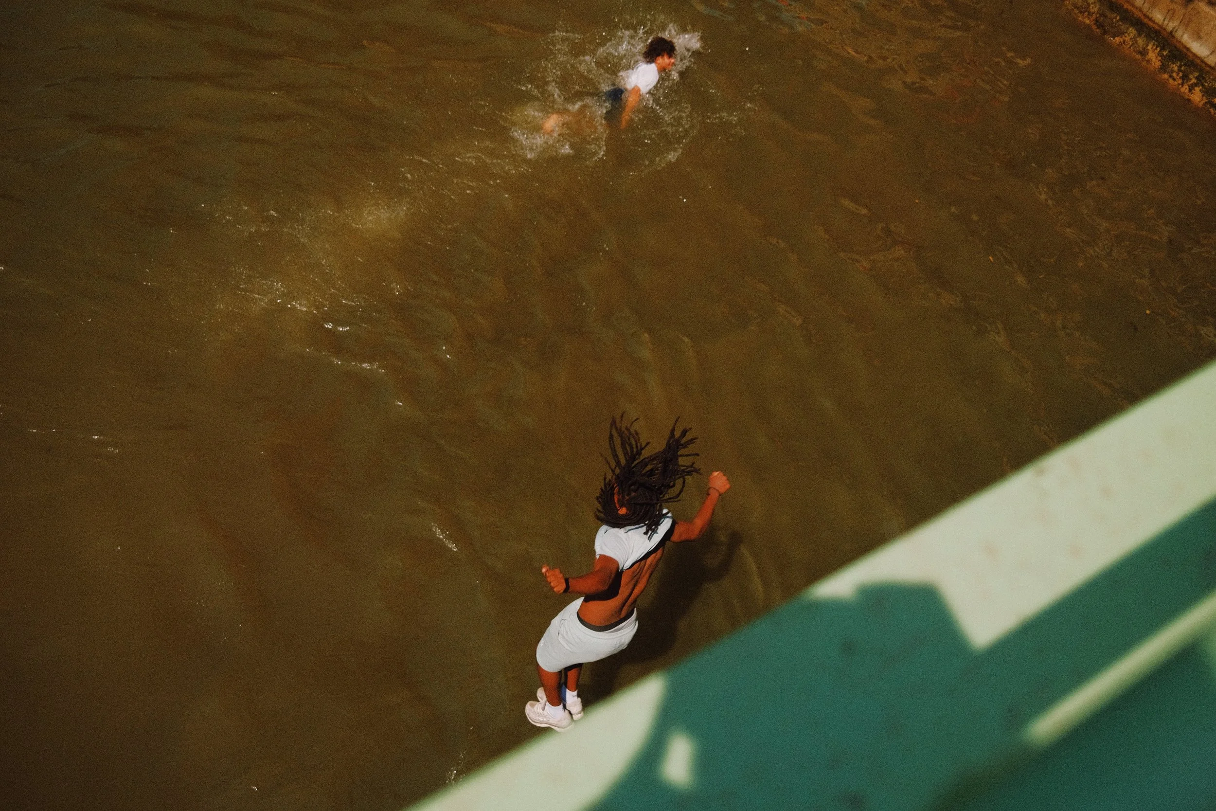 Une personne nage dans une piscine, vu d'en haut, avec une barrière verte en premier plan.