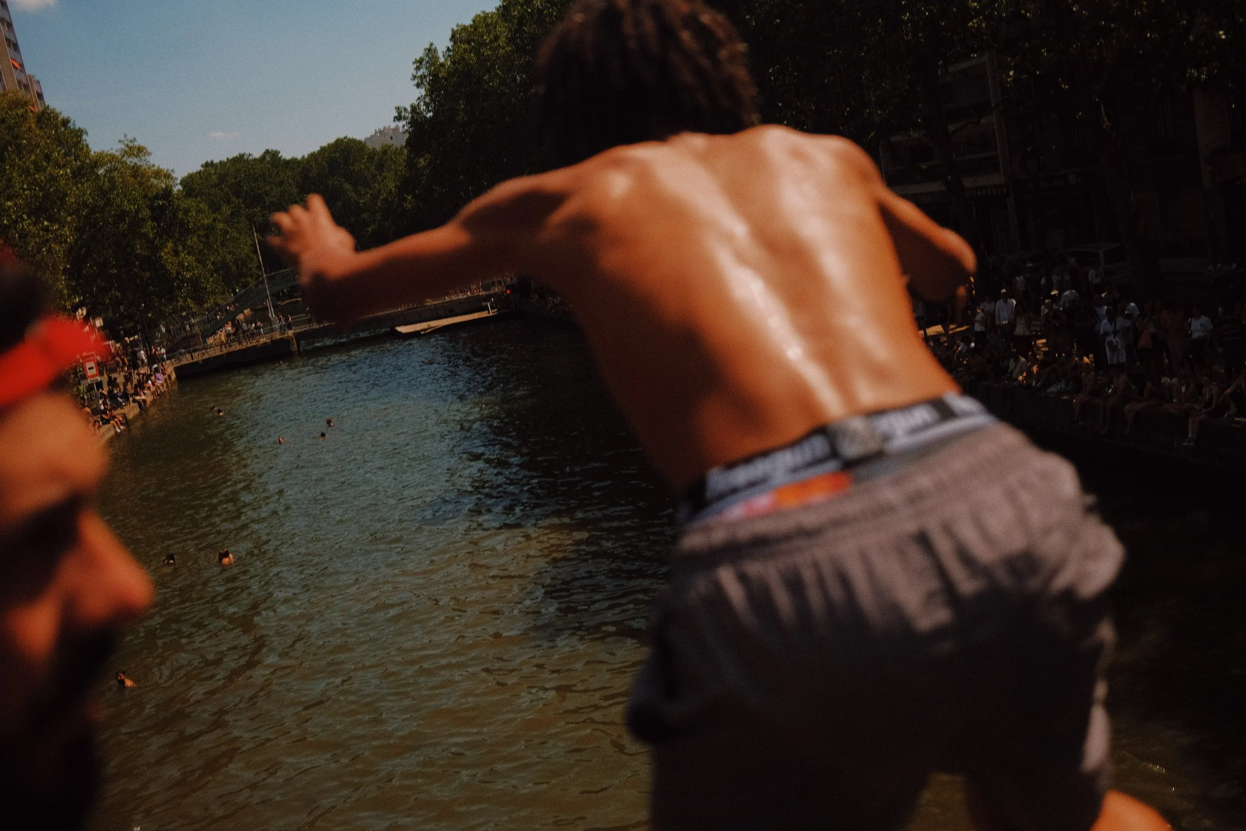 Une personne nue qui saute dans une rivière lors d'un événement public, avec une foule de spectateurs assis sur les rives.