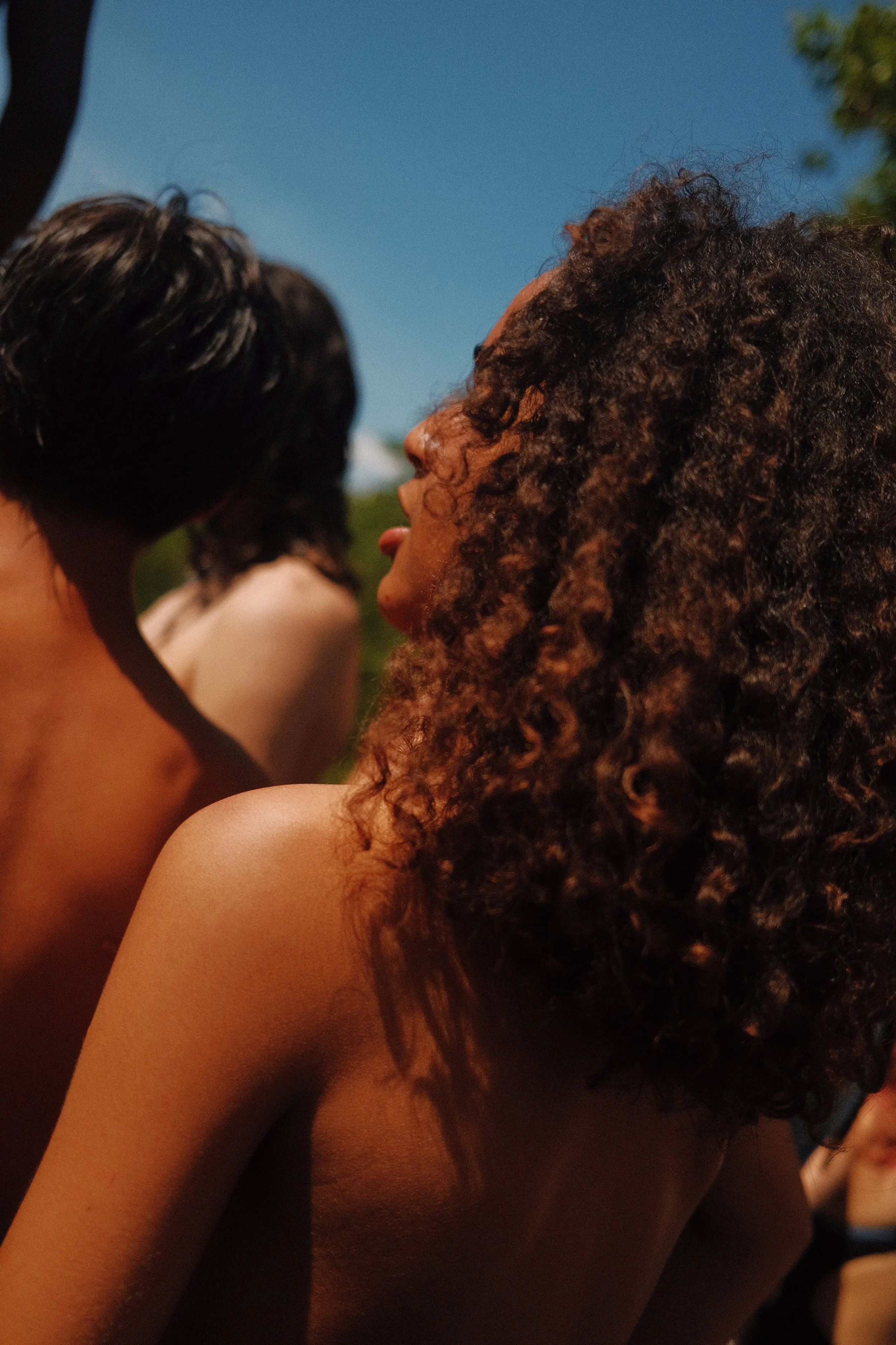 Groupe de personnes nues ou semi-nues, vue de profil, de dos ou de côté, lors d'une activité en extérieur sous un ciel bleu.