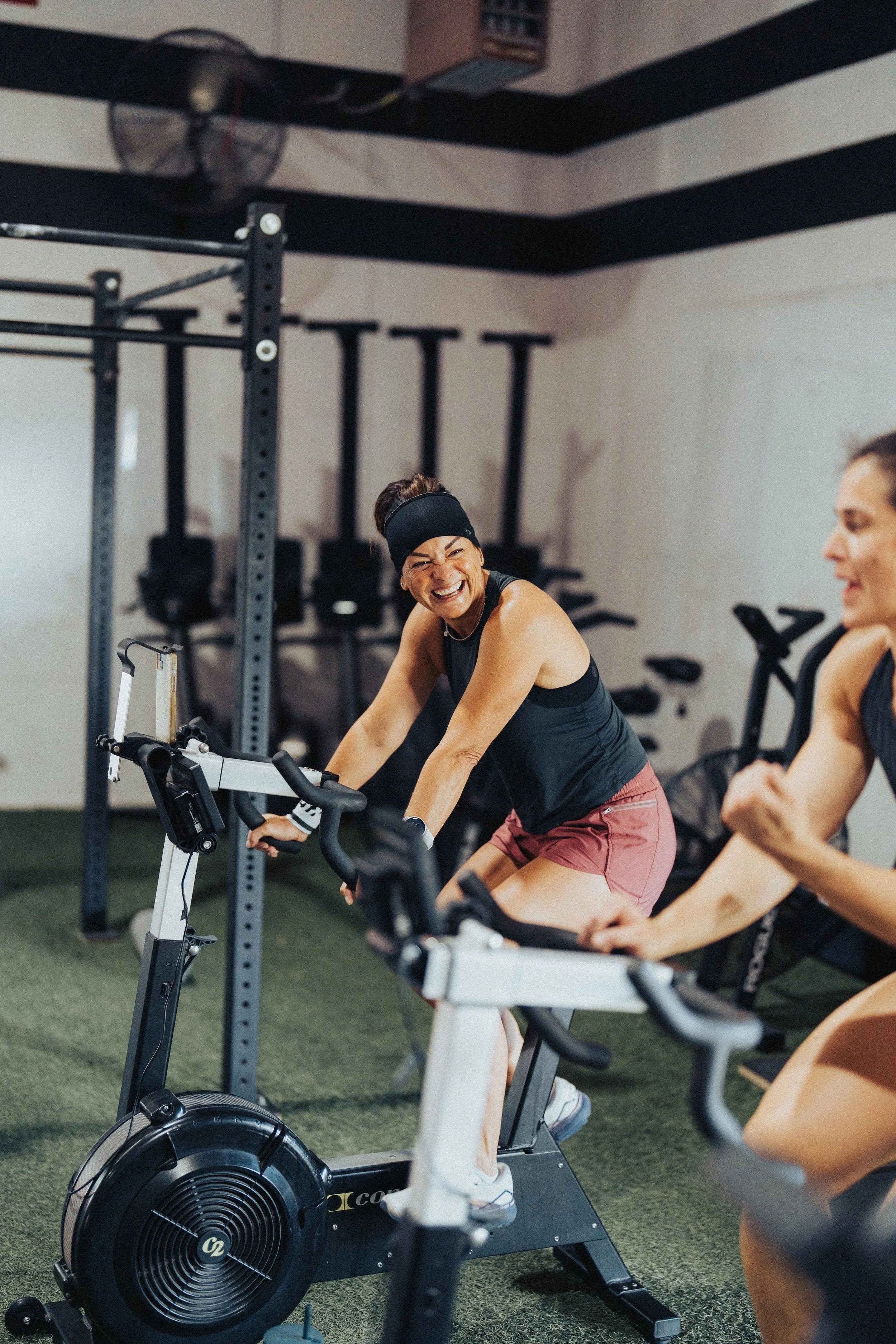 Women participating in a spin class on stationary bikes in a gym, smiling and enjoying the workout.